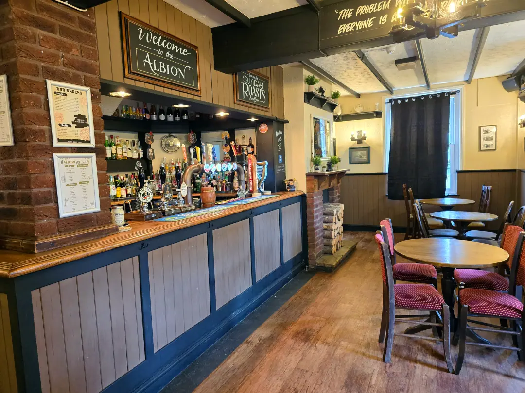 The main bar, with a panelled navy counter, red stools and a Welcome to the Albion board