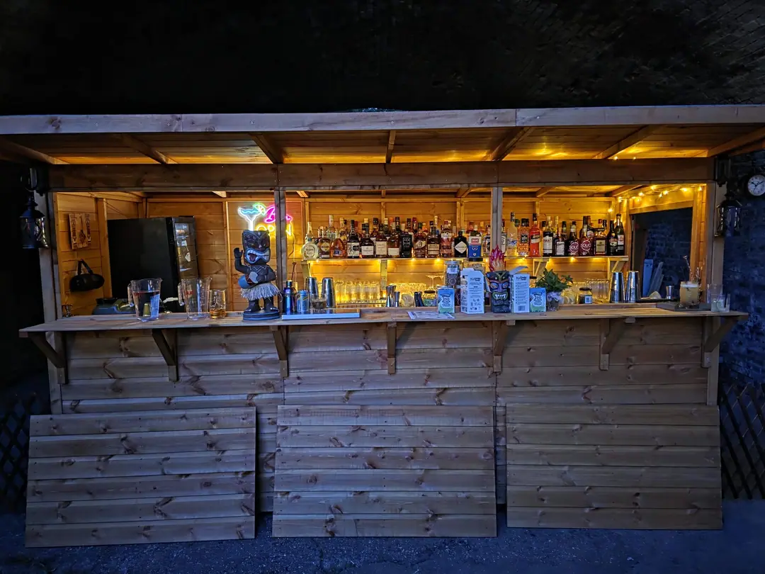 The garden bar under the same arch at night, its shelves of spirits lit in gold