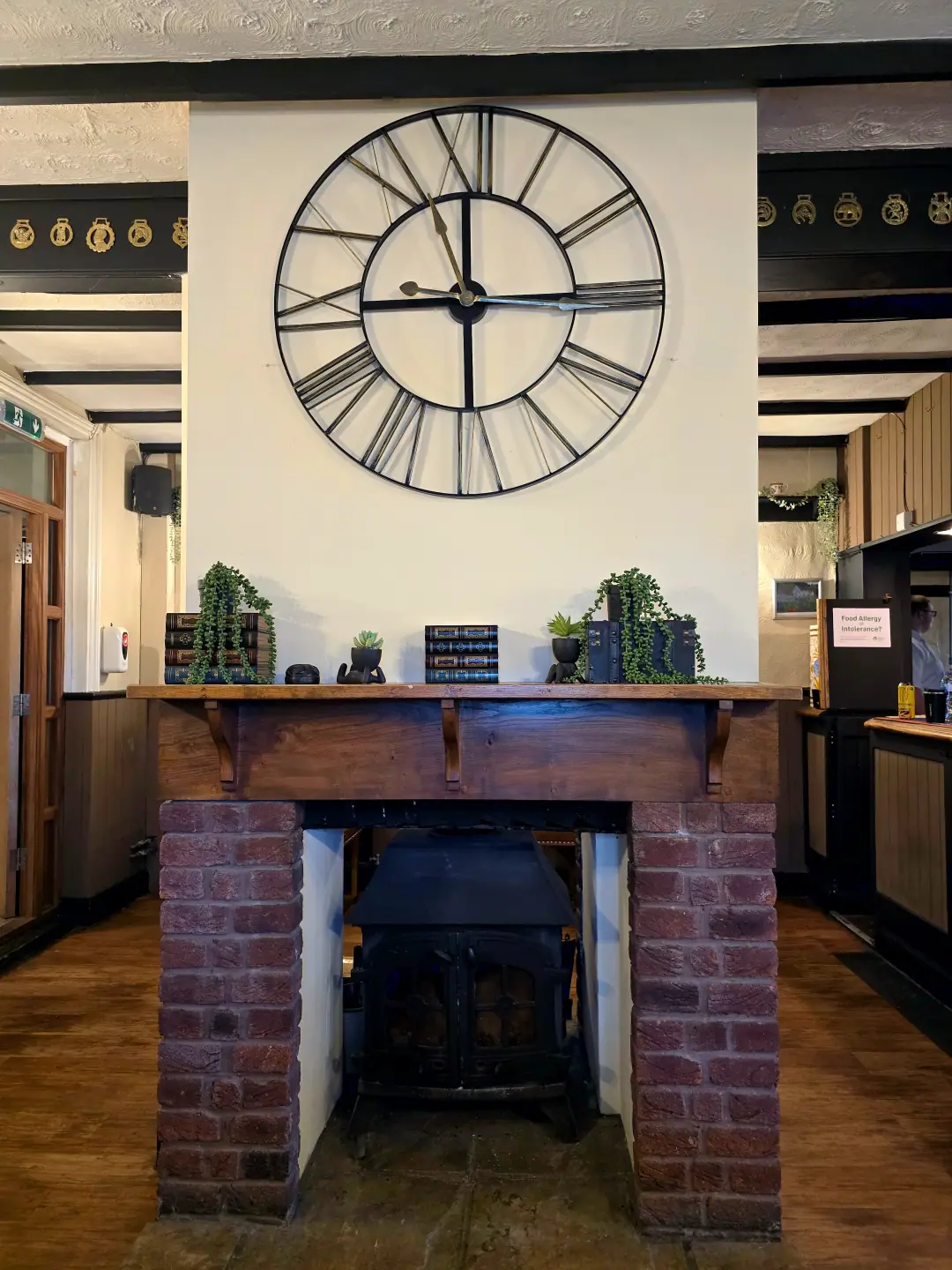 A double-sided stove under an oak mantel, with a giant skeleton clock and horse brasses